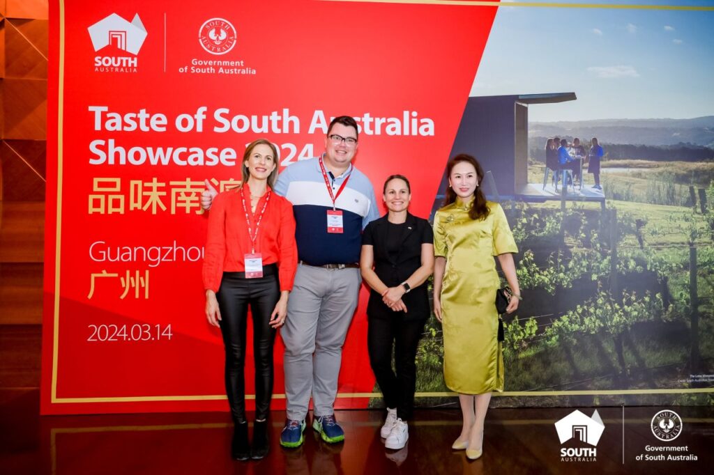 Four people pose in front of a photo wall at the Taste of SA delegation in China