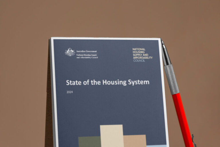 State of the Housing System report with a pen lying against it on a brown background