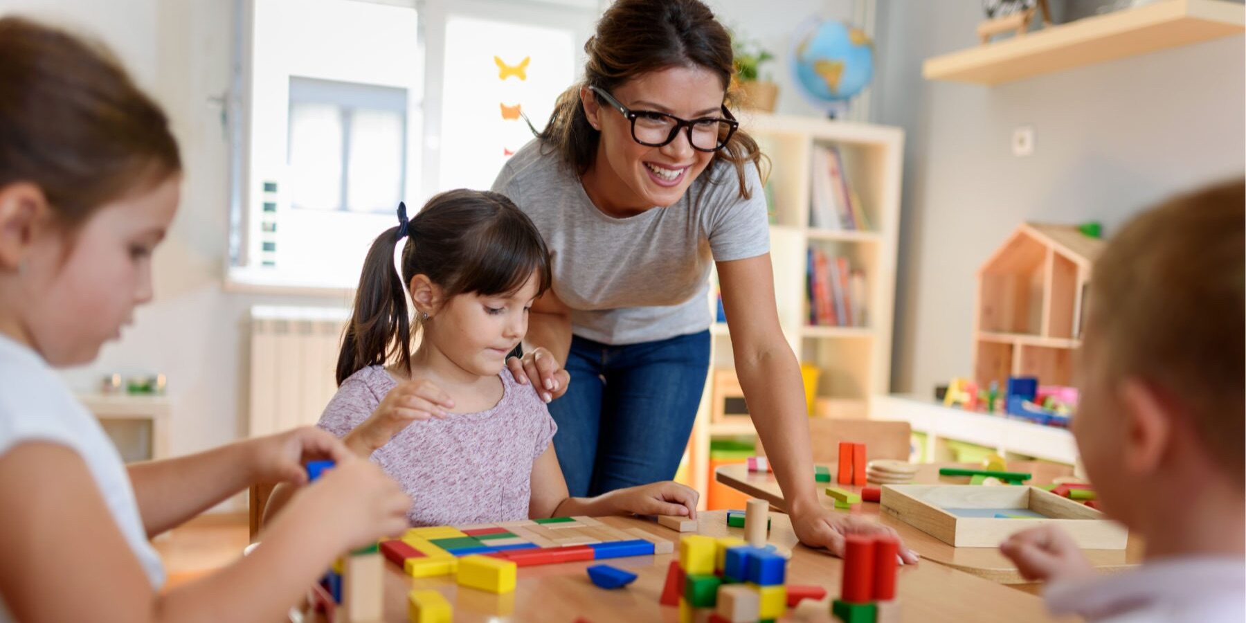 24716933-eafa-3943-4dca-0868b0557f8f An early learning educator with children at a table using blocks.