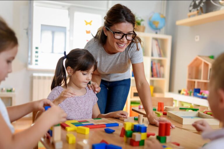 An early learning educator with children at a table using blocks.
