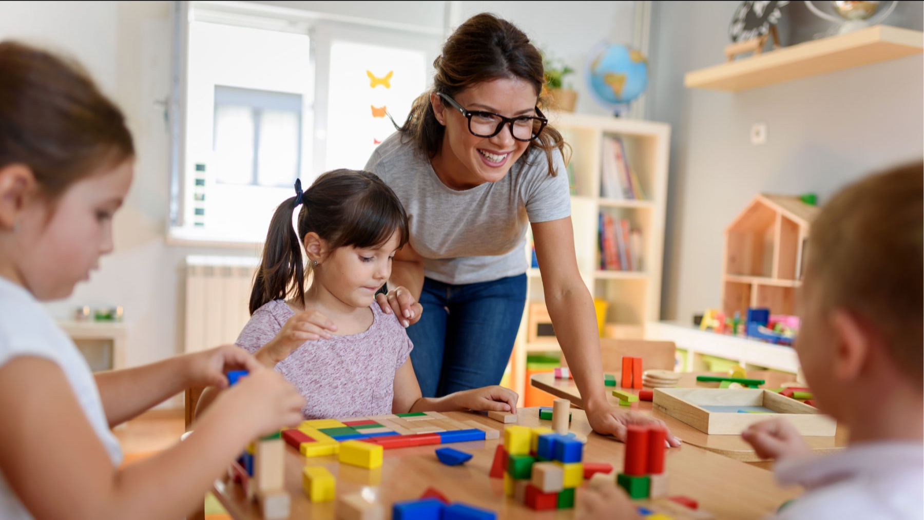 An early learning educator with children at a table using blocks.