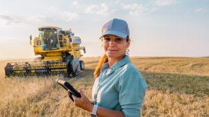 A person stands in a field with farming machinery behind them.