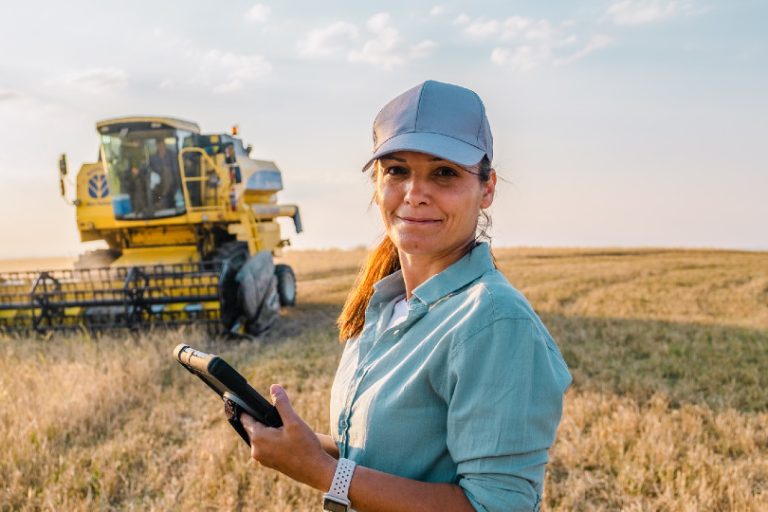 A person stands in a field with farming machinery behind them.