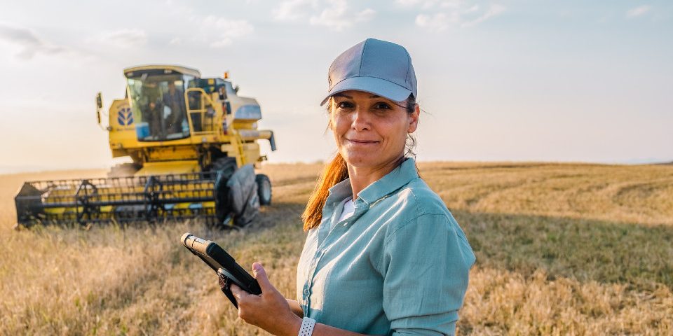 funding-support A person stands in a field with farming machinery behind them.